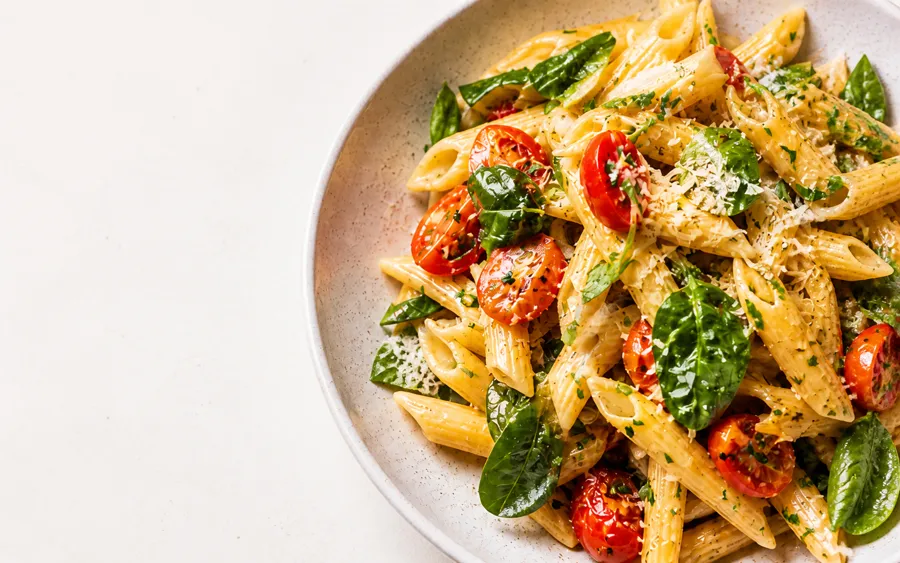 A bowl of penne with tomatoes, spinach and basil